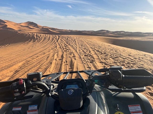 Quad handlebars facing a dune valley criss-crossed with tyre tracks
