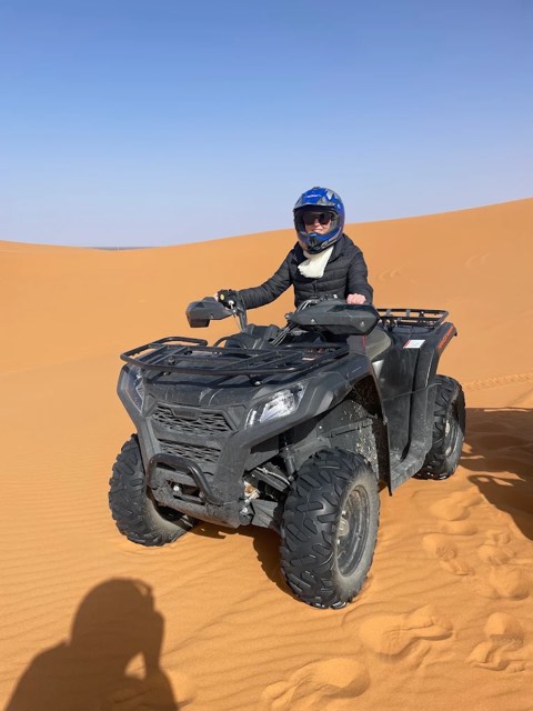 Rider in a full-face helmet on a black quad bike on soft sand