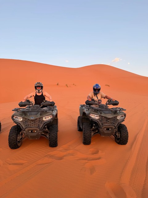 Two riders on quad bikes side by side among orange dunes in Merzouga