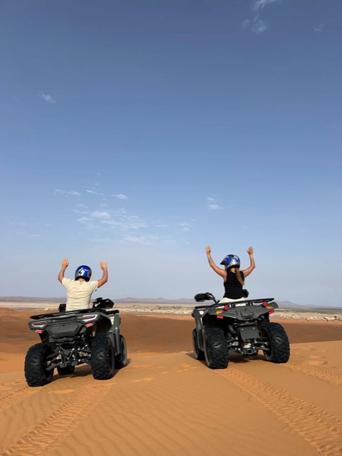 Two quad riders raising their arms on a dune ridge in the Sahara